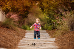 30A family portrait — candid running toddler-boy boardwalk portrait through the pink muhly grass; photographed by Amanda Eubank Photography along Florida’s Emerald Coast.