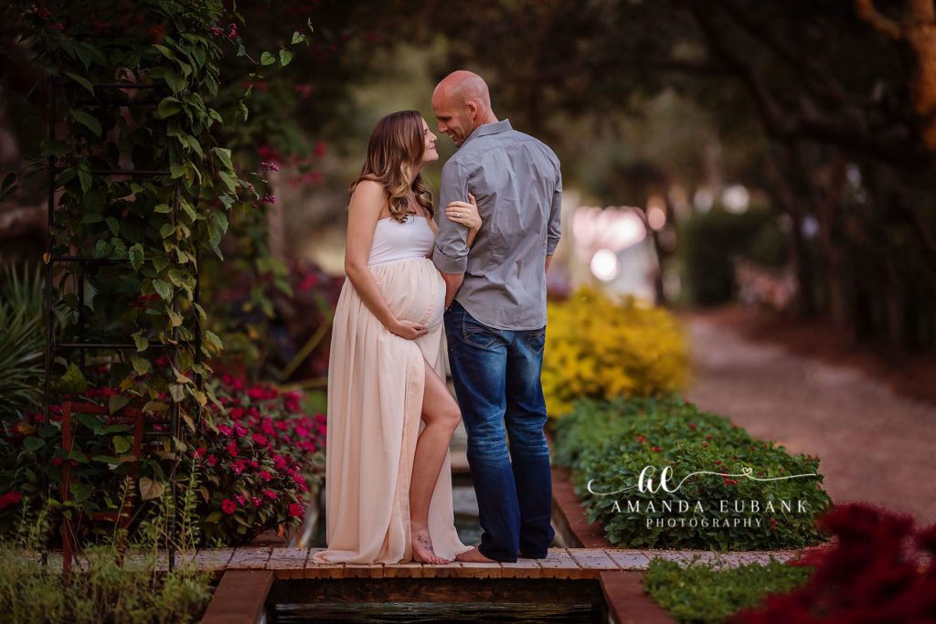 30A maternity portrait — standing forehead-to-forehead blush-gown maternity portrait on the garden bridge; photographed by Amanda Eubank Photography along Florida’s Emerald Coast.