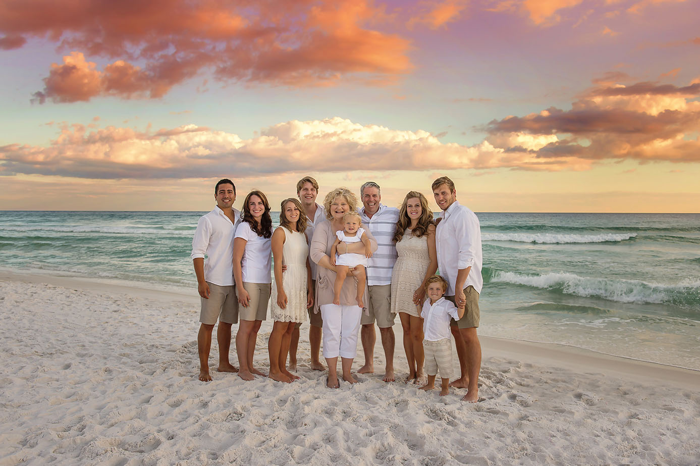 Alys Beach Extended-Family-of-Nine Pastel Sunset Portrait — Alys Beach Family Photographer Extended family of nine in coordinated whites, khakis, and creams standing together at the Alys Beach shoreline beneath a soft peach, pink, and lavender pastel sunset; photographed by Amanda Eubank Photography along Florida’s Emerald Coast.