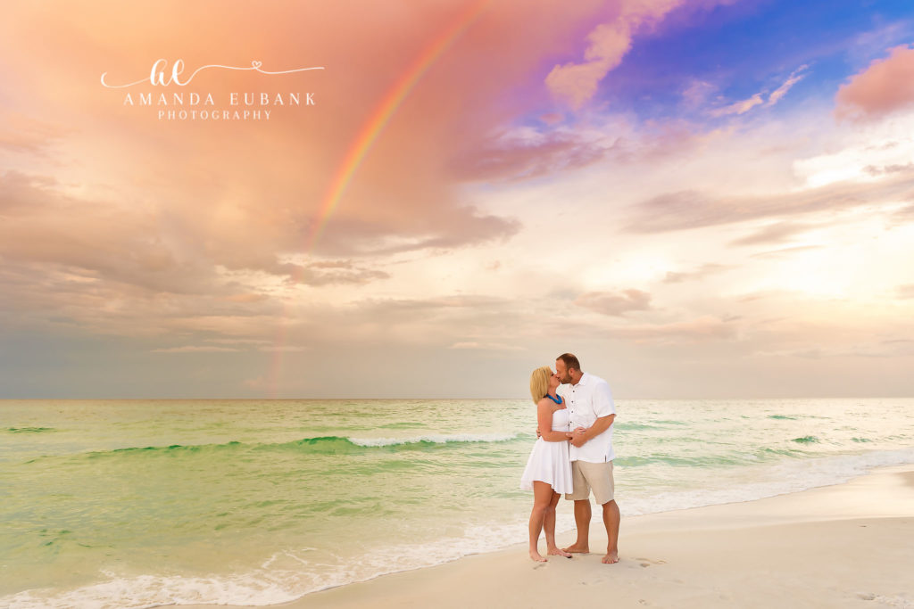 Couple kissing under a sunrise rainbow on the beach with white attire