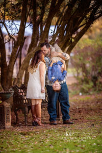 Santa Rosa Beach area family portrait of mom and son — a tender mother-and-son moment at Eden Gardens with mom in her white lace minidress and cognac boots seated on a white painted veranda railing while she snuggles her son in a chambray button-down and khakis close to her chest, eyes closed; photographed by Amanda Eubank Photography along Florida's Emerald Coast.