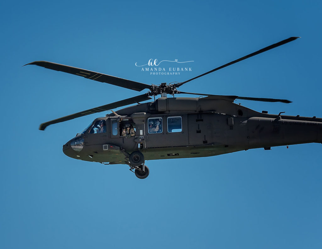 U.S. Army UH-60 Black Hawk helicopter in flight against a clear blue sky — side-view pass with crew visible