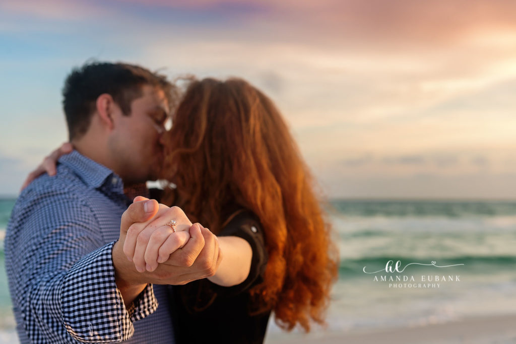 Surprise beach proposal on Destin Florida sand — red-haired bride-to-be and fiancé in blue gingham — embrace at the tide line