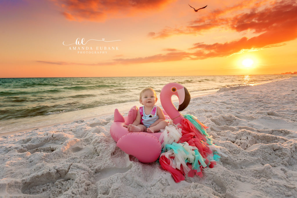 Sybi grinning from inside her pink flamingo float as a bird flies through the fiery sunset over Miramar Beach.