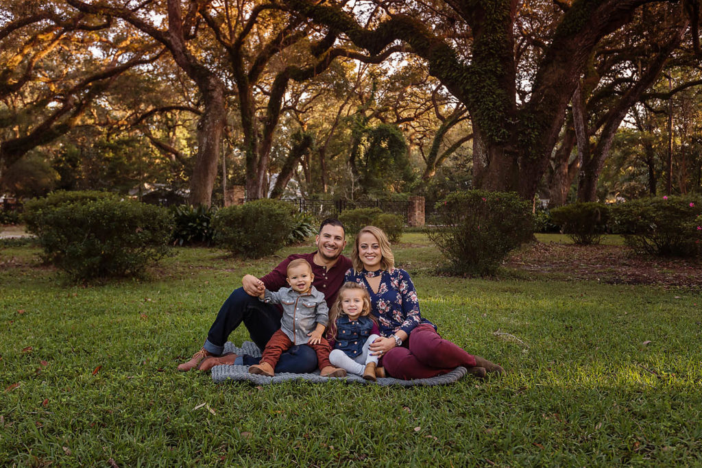Prieto family of four cuddled together on a blanket beneath the oak trees at Eden Gardens