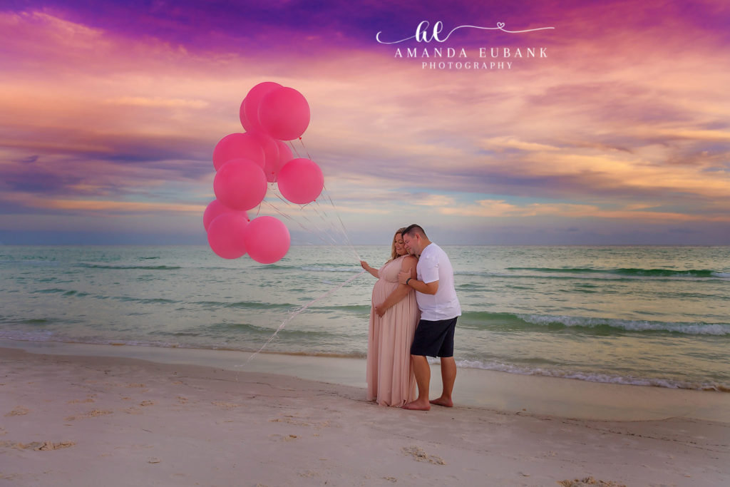 30A Florida maternity photographer captures expecting couple with pink balloons on beach at vibrant sunset Seaside