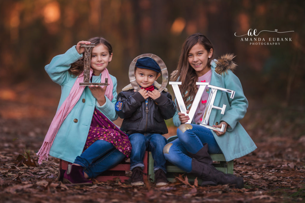 tight portrait of the aviator boy with his biplane during a Friendswood winter forest sibling mini-session on a Friendswood pine forest in golden autumn light, photographed by Amanda Eubank Photography in golden-hour woodland light with candid documentary frame.
