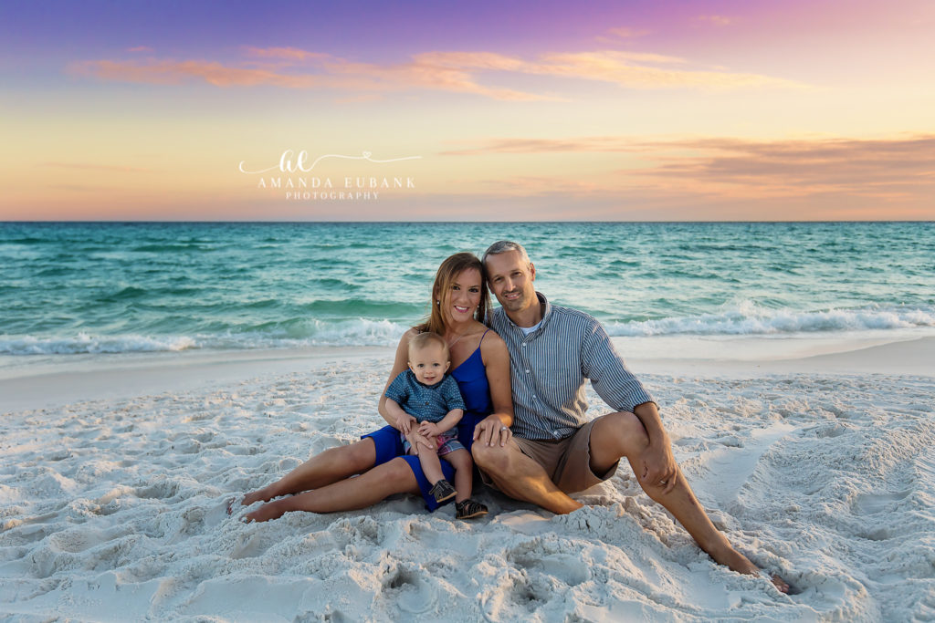 the toddler grinning over mom's shoulder during a Destin sunset mother-and-toddler session on Destin Beach in lavender sunset, photographed by Amanda Eubank Photography