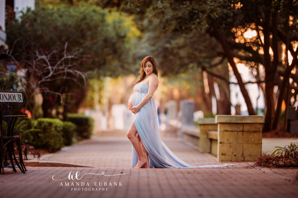 30A Florida maternity photographer captures redhead mom-to-be in light blue gown on Seaside brick walkway