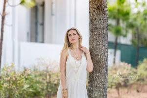 Poised editorial brand portrait of a model in a cream slip dress posed against a soft greenery hedge captured under warm coastal glow