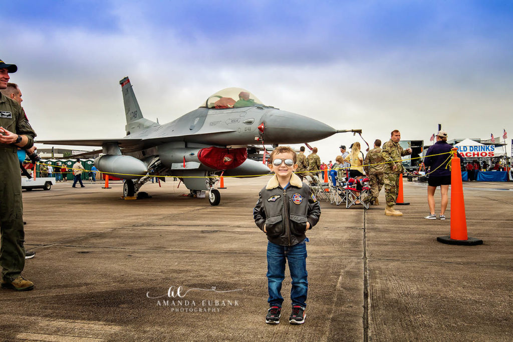 Documentary photograph of child explorer admiring a static-display warbird on the airfield tarmac during the Wings Over Houston Air Show in Texas
