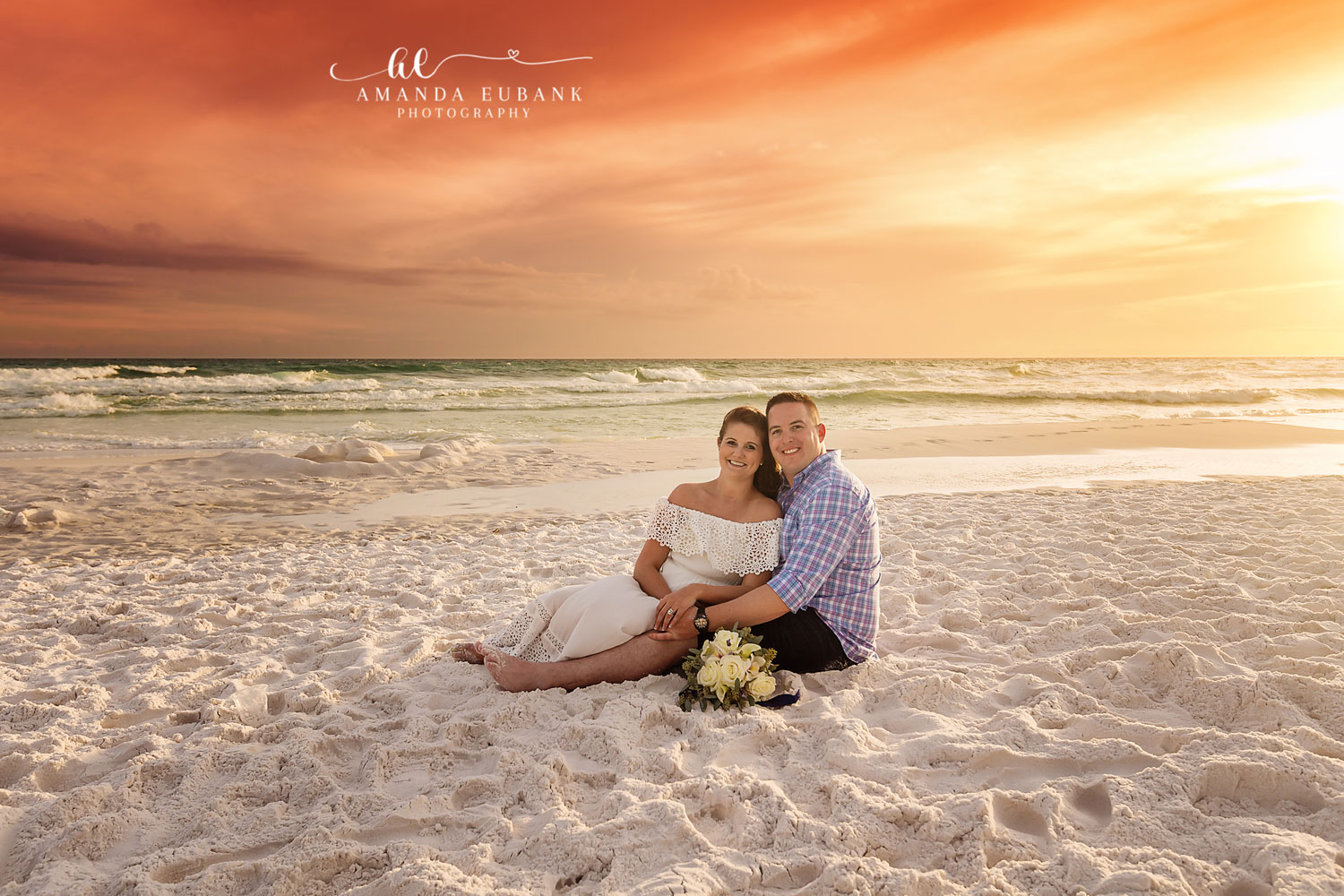 Seagrove Beach Florida Engagement Photographer — Couple on the Sand at Fiery Sunset Engaged couple sitting on the sand with a white bouquet under a fiery orange sunset sky in Seagrove Beach, Florida.
