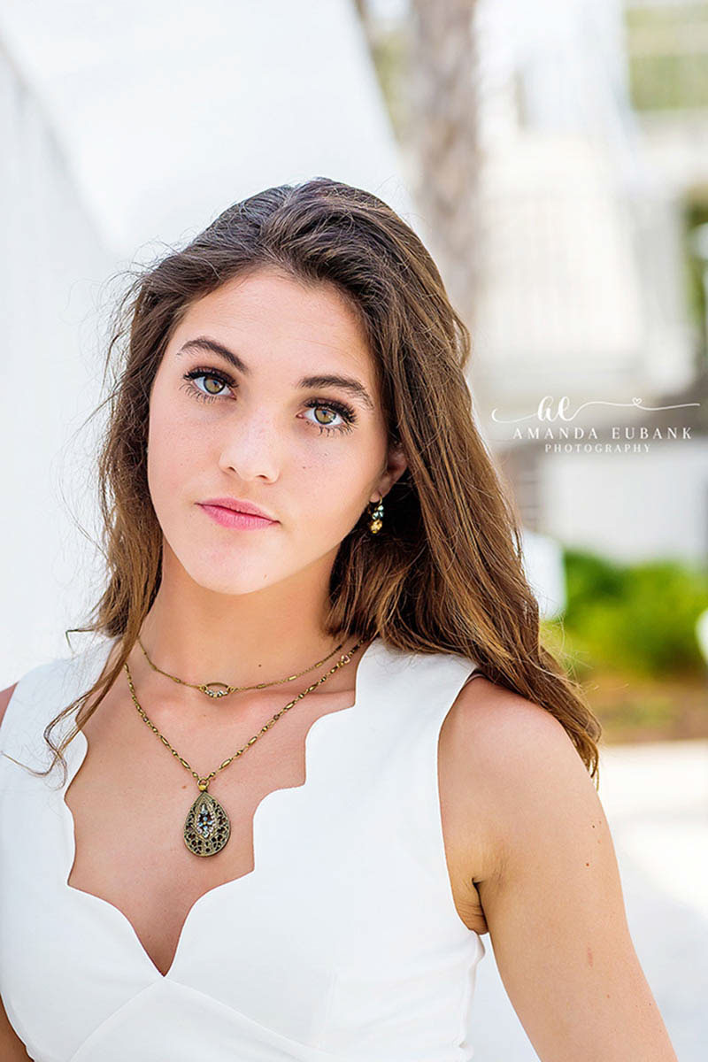Brunette high school senior in a white scalloped top with a green pendant during her senior portrait session along 30A Florida