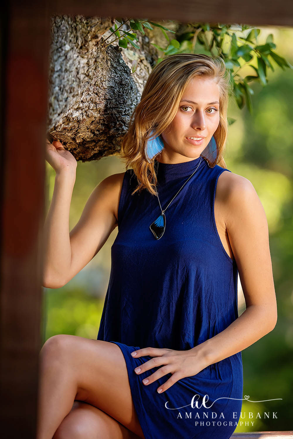 Blonde high school senior in a navy romper standing beside a tree during her senior portrait session in Alys Beach, Florida along 30A