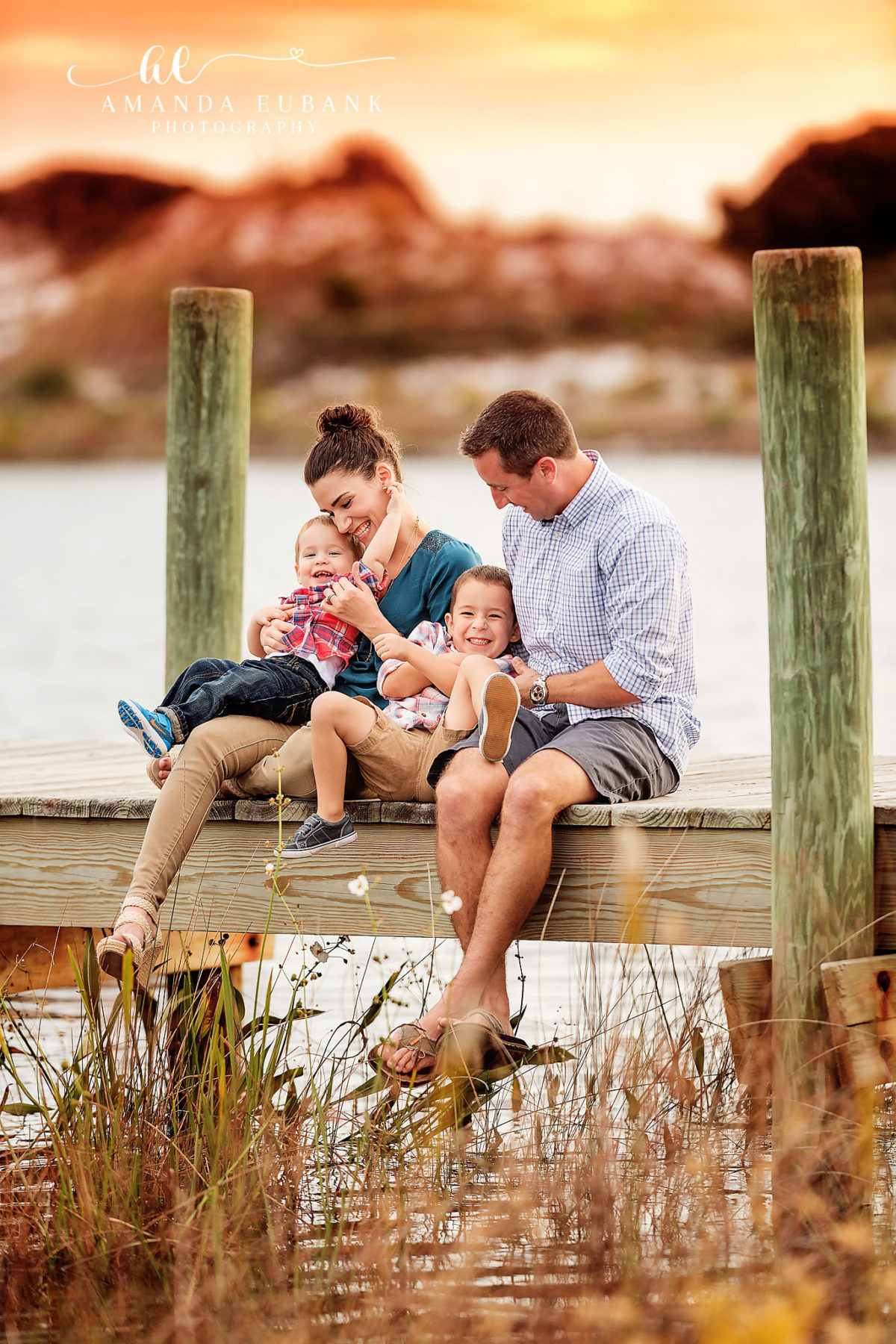 Watersound Florida Family Photographer — Family of Four on the Dune Lake Dock at Sunset Family of four sitting together on a wooden dock at the coastal dune lake at golden sunset in Watersound, Florida.