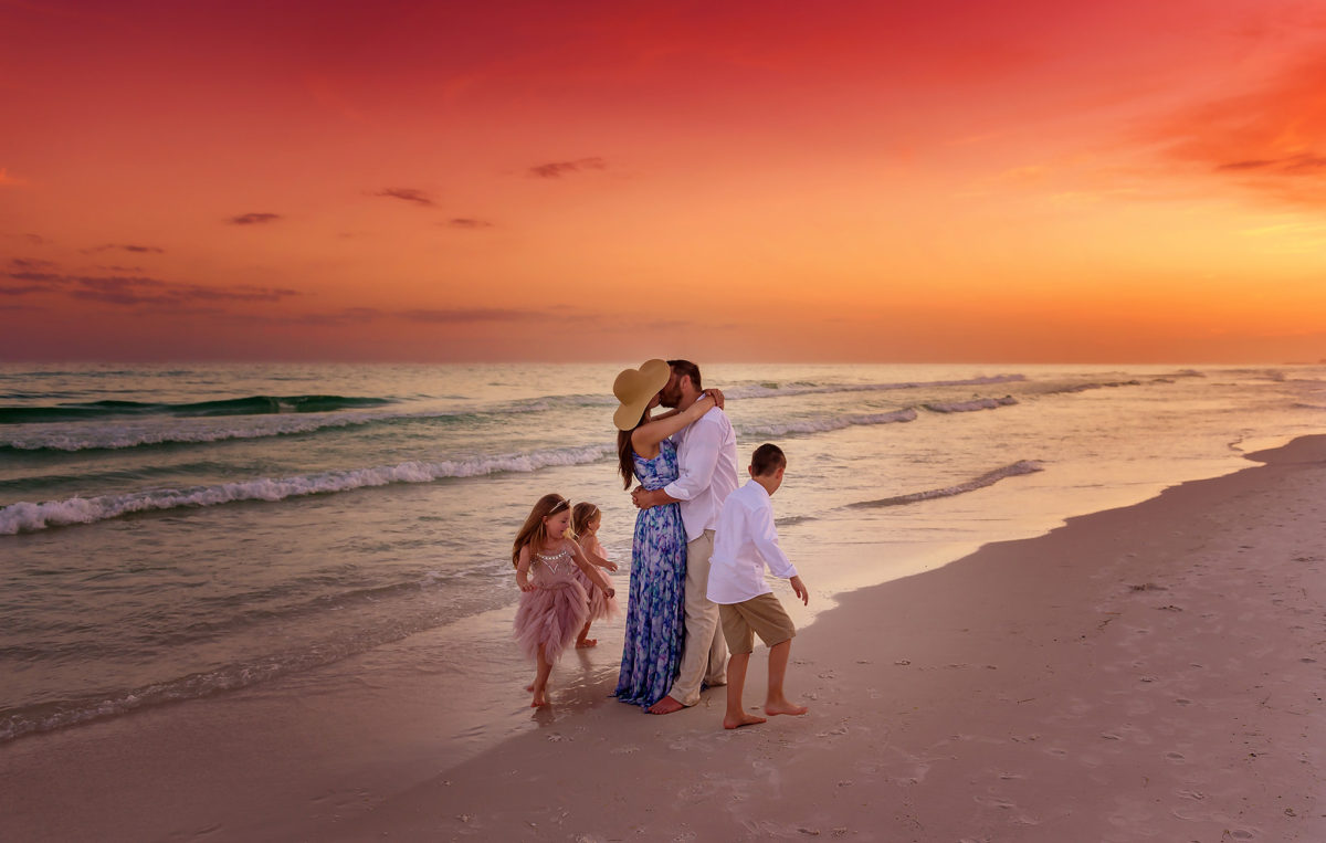Santa Rosa Beach Family Photographer – Sunset Beach Session A family of seven walking together on Santa Rosa Beach at sunset with a vibrant orange and pink sky.