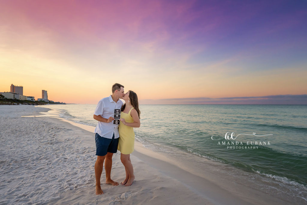 Sarah and her husband sharing a tender moment as she cradles her baby bump at the 30A shoreline in ocean-mist twilight