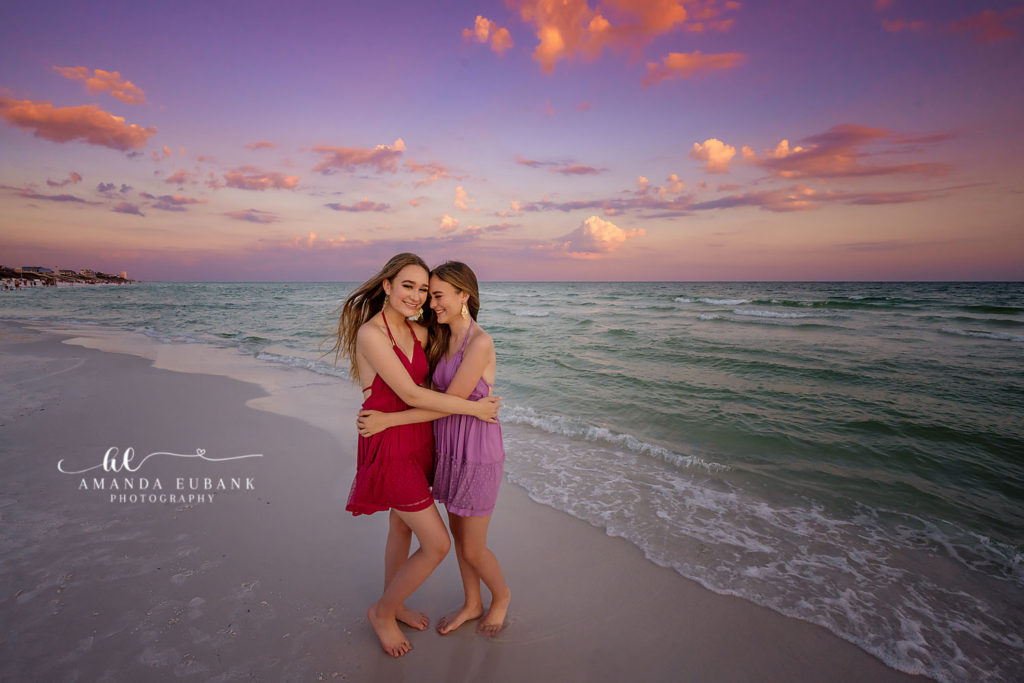 Twins side by side on the shoreline beneath cotton clouds drifting at last light