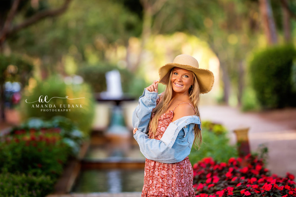 Alyssa looking out across the dunes in the straw hat as sea oats sway beneath a peach sunset sky