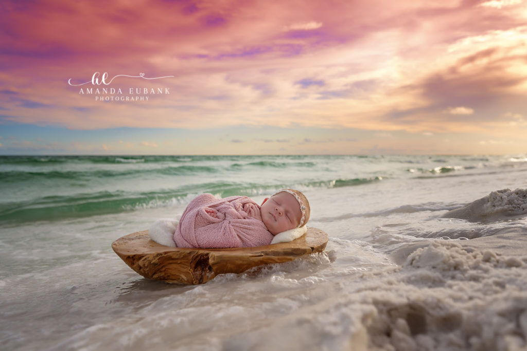 Baby S sleeps in a soft swaddle with the gulf shoreline behind her at sunset