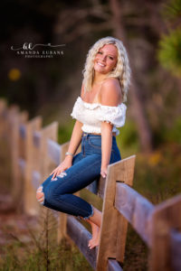 Ali leaning on the boardwalk bridge rail in her lilac romper at sunset.