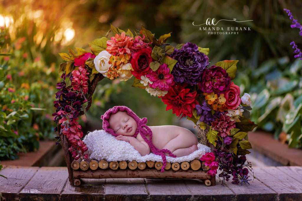 Watercolor newborn photographer captures Baby Saylor curled up on a wooden bed under autumn florals