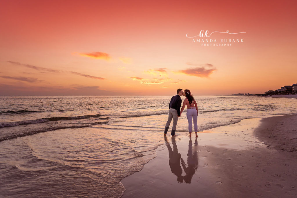 The Kennedys kissing on the wet 30A shoreline with their reflection in the sand at magenta sunset.