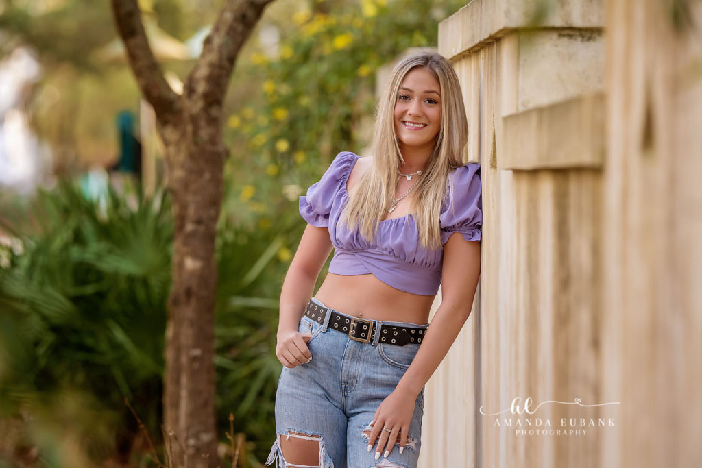 Faith leaning against a Rosemary Beach garden fence in a lavender puff-sleeve crop top and ripped denim.