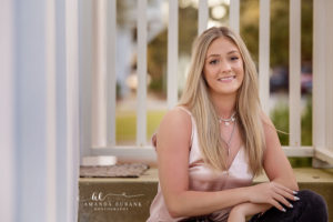 Faith seated against a crisp white slat fence with green park bokeh during her Rosemary Beach senior session.
