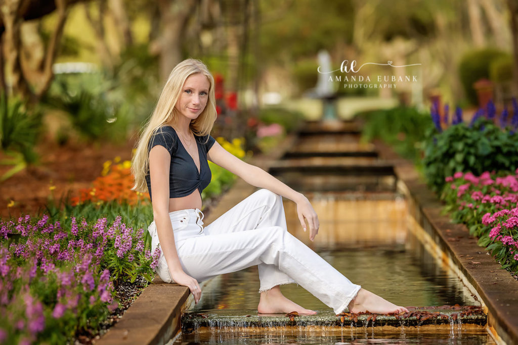 Ava leaning against a tree in her black crop top and white jeans in the Watercolor gardens.