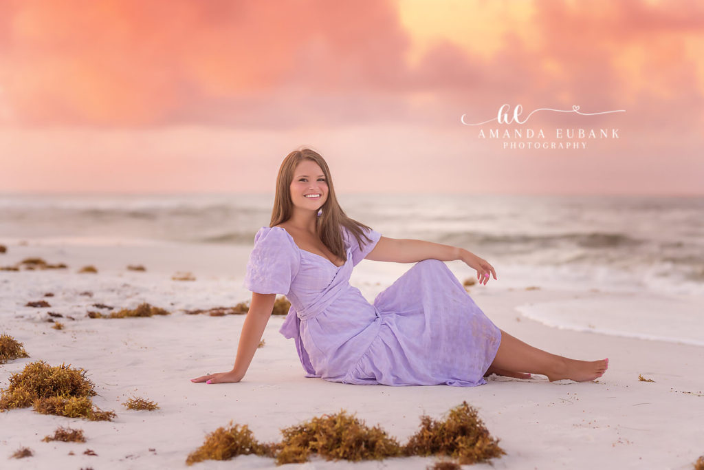 Ava in a tender pose on the Watercolor beach in a lavender midi dress with rosy dawn light around her.