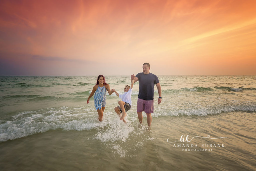 F Family mom laughing in the surf at Rosemary Beach in her tie-dye blue dress at sunset.