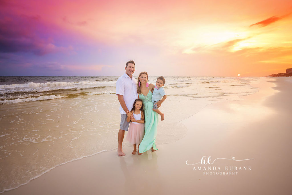 H Family parents sharing a quiet kiss as the kids play in the Seacrest Beach sand nearby.
