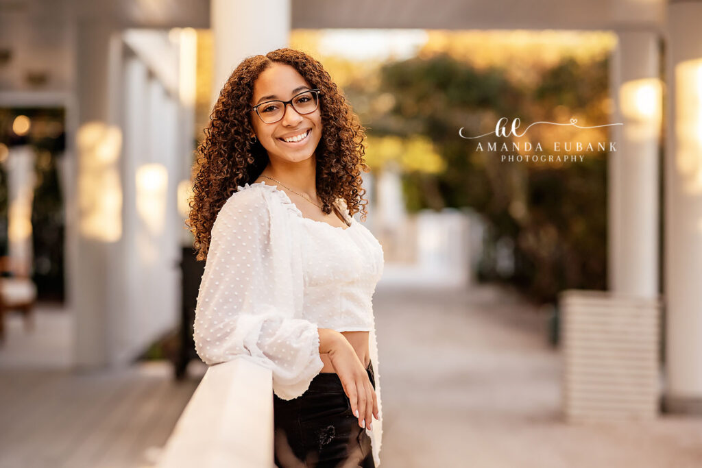 J leaning playfully on a sea-oat beach dune at golden hour during her Watercolor senior session.