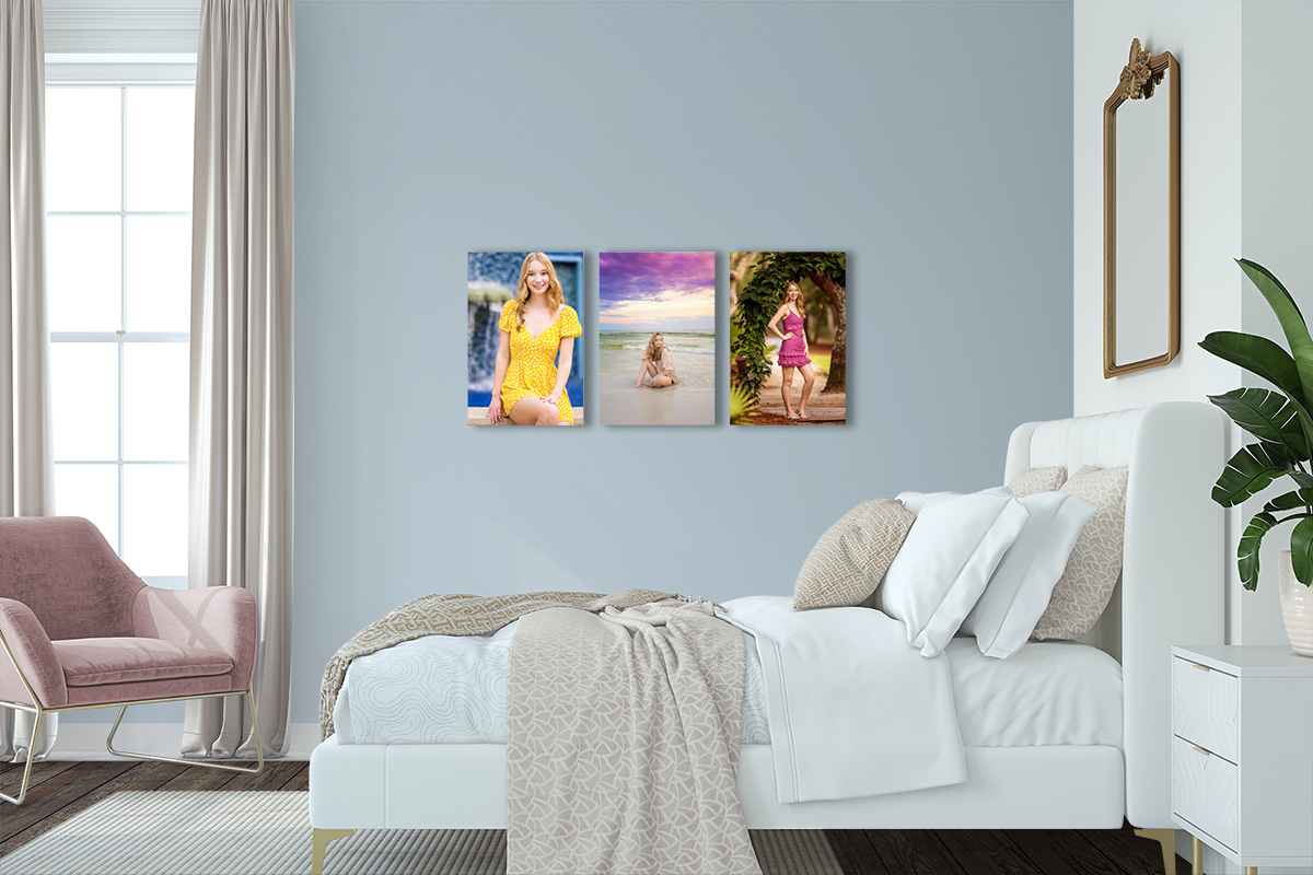 30A Senior Portrait Triptych Wall Art — Pastel Bedroom A three-panel canvas wall display of vibrant senior portraits in yellow and magenta dresses hung above a white bed in a pastel-blue bedroom.