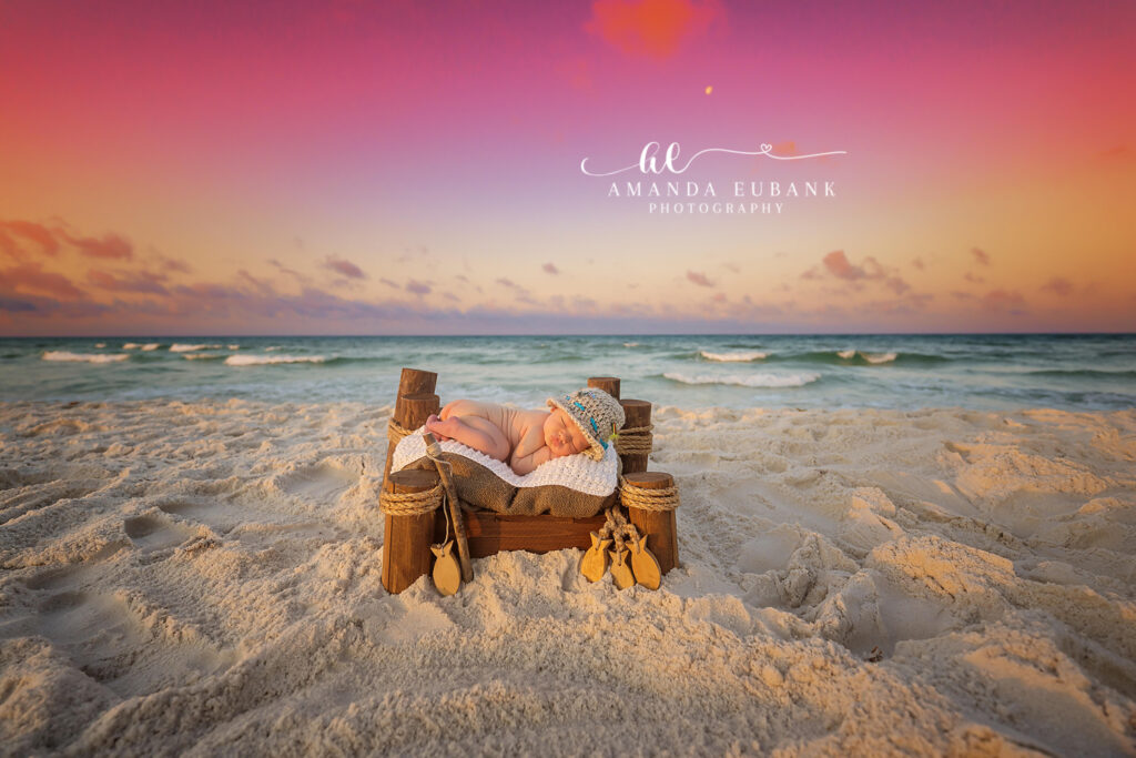Newborn baby curled in a tiny driftwood bed on the beach during a beachside Rosemary Beach newborn session at raspberry-and-tangerine sunset.