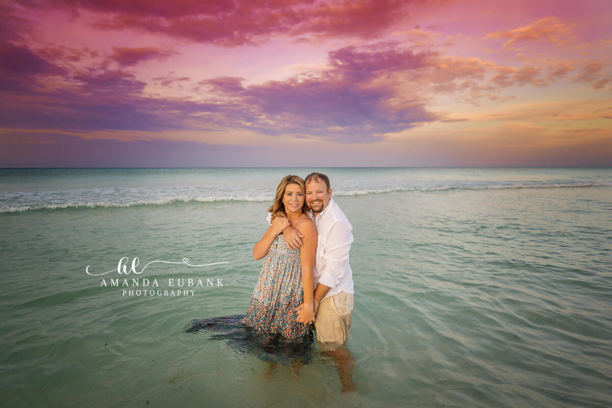Seaside Sunrise Couple Session 16 A couple kisses at the shoreline at dawn with the dramatic dawn sky overhead during painted sunset sky.