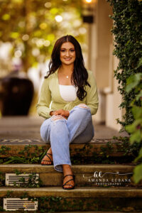 Senior Ava seated on the brick steps in her sage green wrap top during her town session