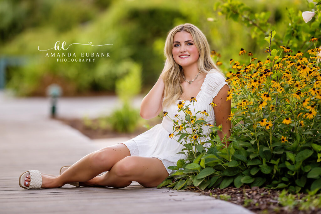 Ella in a soft white smocked sundress framed by golden sunlight in a Rosemary Beach garden tucked between elephant ear plants.