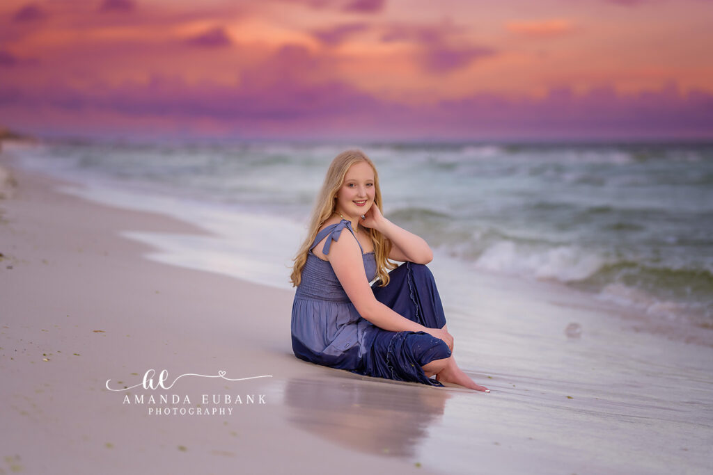 Sunset wave portrait of Mallory in her red lace dress with warm golden light wrapping around the shoreline.