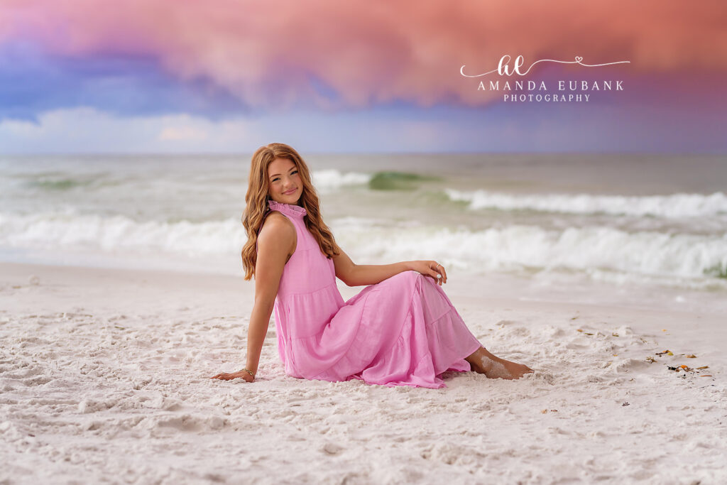 Sunset Beach Reflection — the redheaded senior in a soft pink tiered maxi dress along the white sand of a Watercolor Beach sunset shoreline.
