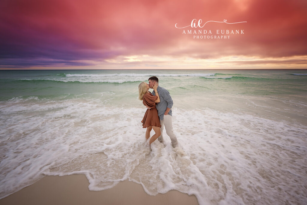 Man dipping the woman backward for a kiss as small waves crash behind them on the beach