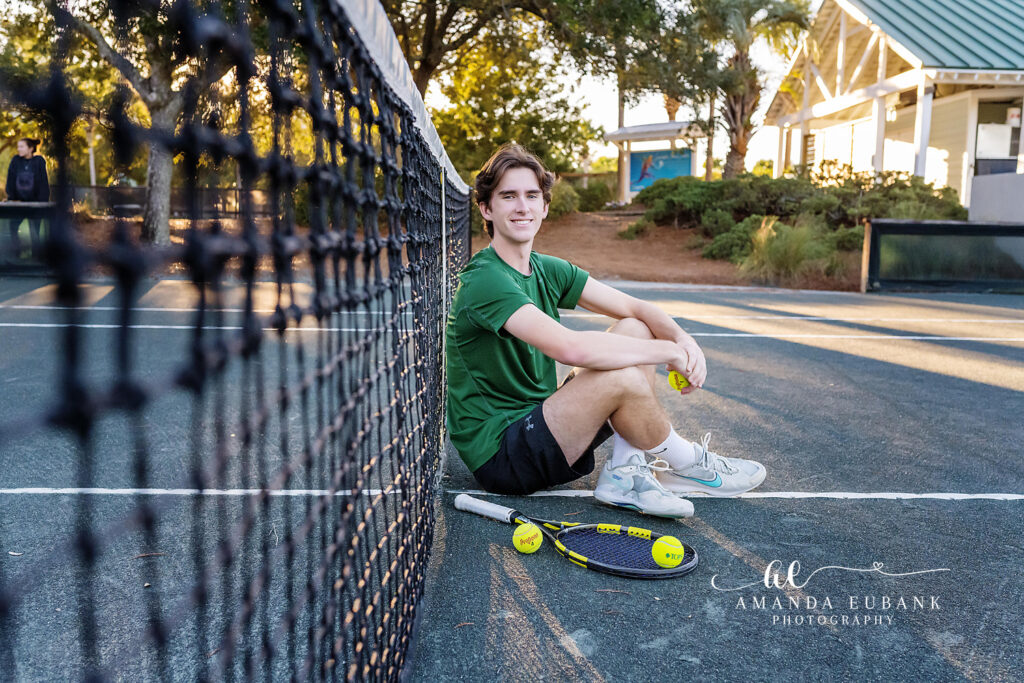 Black and white marina portrait of a senior boy beside a chalkboard sign on a wooden walkway