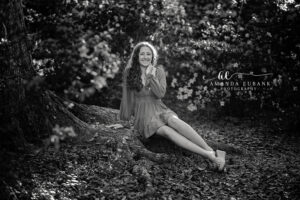 Black and white portrait of a senior girl seated in a flower-filled garden by a tree
