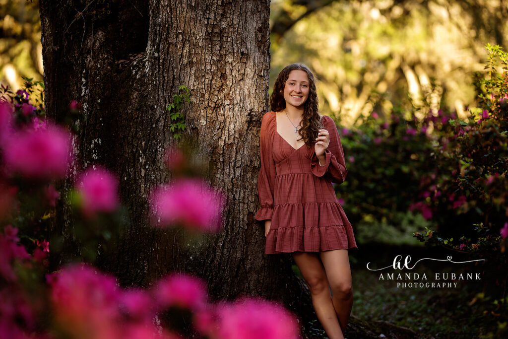 Senior girl in a rust dress posed near pink blooming garden flowers