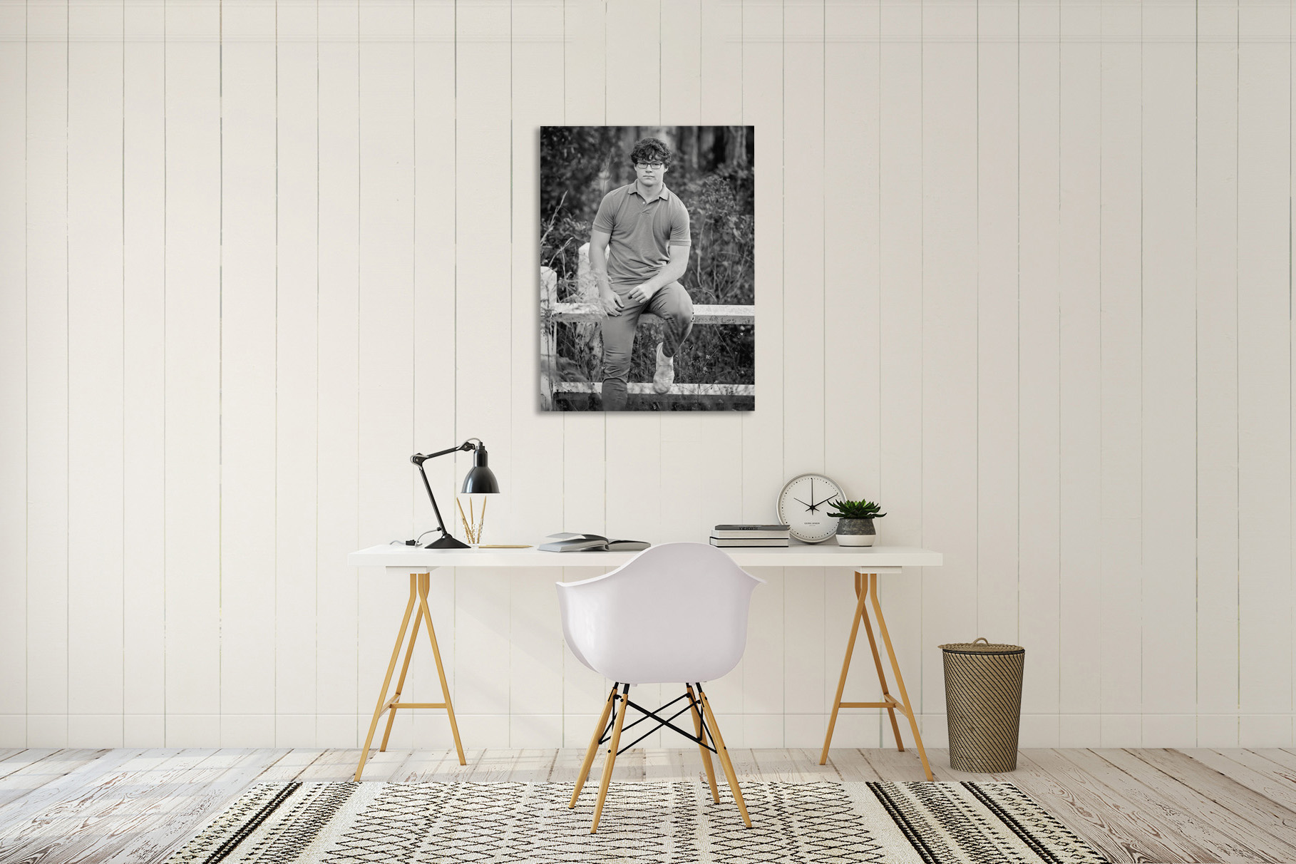 Single black-and-white senior portrait of a young man on a fence, displayed as canvas wall art above a styled white desk