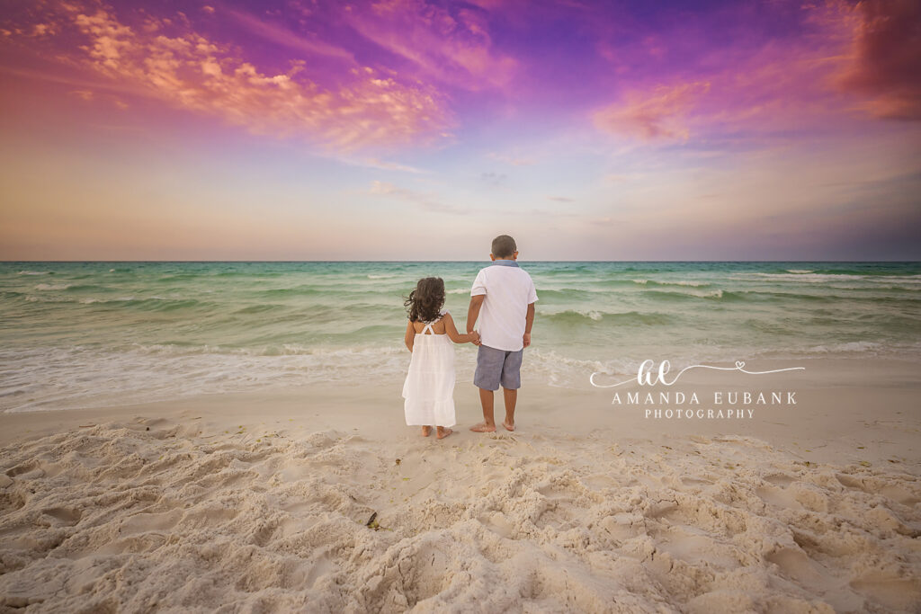 Matriarch and patriarch share an embrace at sunrise in a red maxi and white linen shirt on the soft Destin beach beneath a vibrant pink and orange sky.
