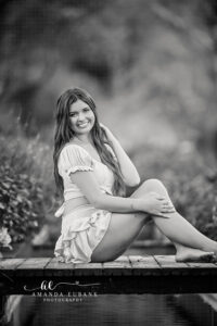 Watercolor sunrise senior Miss R head tilted with a sweet smile beside the koi-pond bridge railing, yellow ruffles framing her in the garden, in buttery yellow off-shoulder ruffle two-piece set with matching tiered ruffle mini skirt | Watercolor FL Sunrise Senior Portrait Photographer