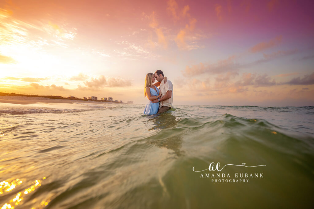 Newly engaged couple standing waist-deep in the Gulf with foreheads touching beneath a glowing golden sunset on 30A
