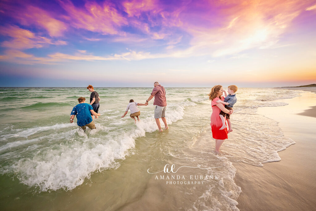G family walks together through the shallow emerald Gulf surf at Destin as small waves lap at their feet beneath a pastel sunset.